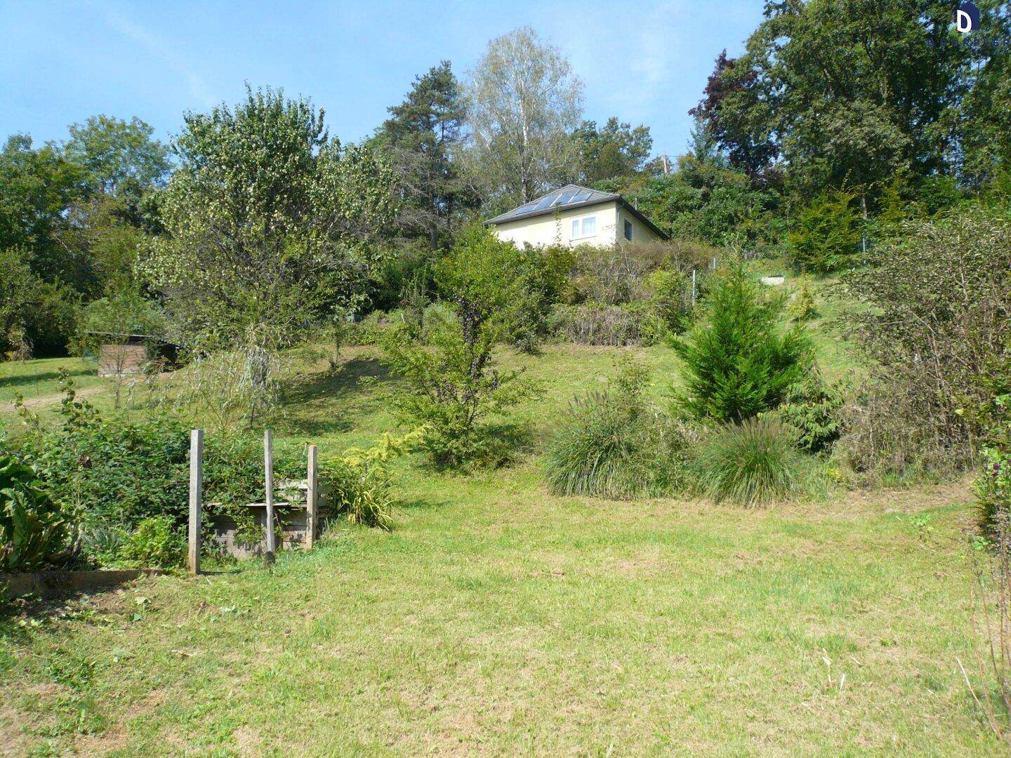 Das Haus liegt eingebettet in eine grüne, hügelige Landschaft mit Bäumen und Sträuchern.