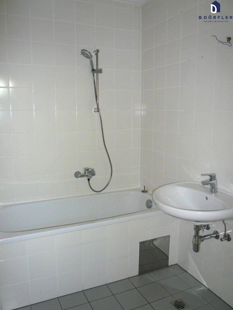 Badezimmer mit Badewanne, Dusche und Waschbecken in hellen Fliesen.