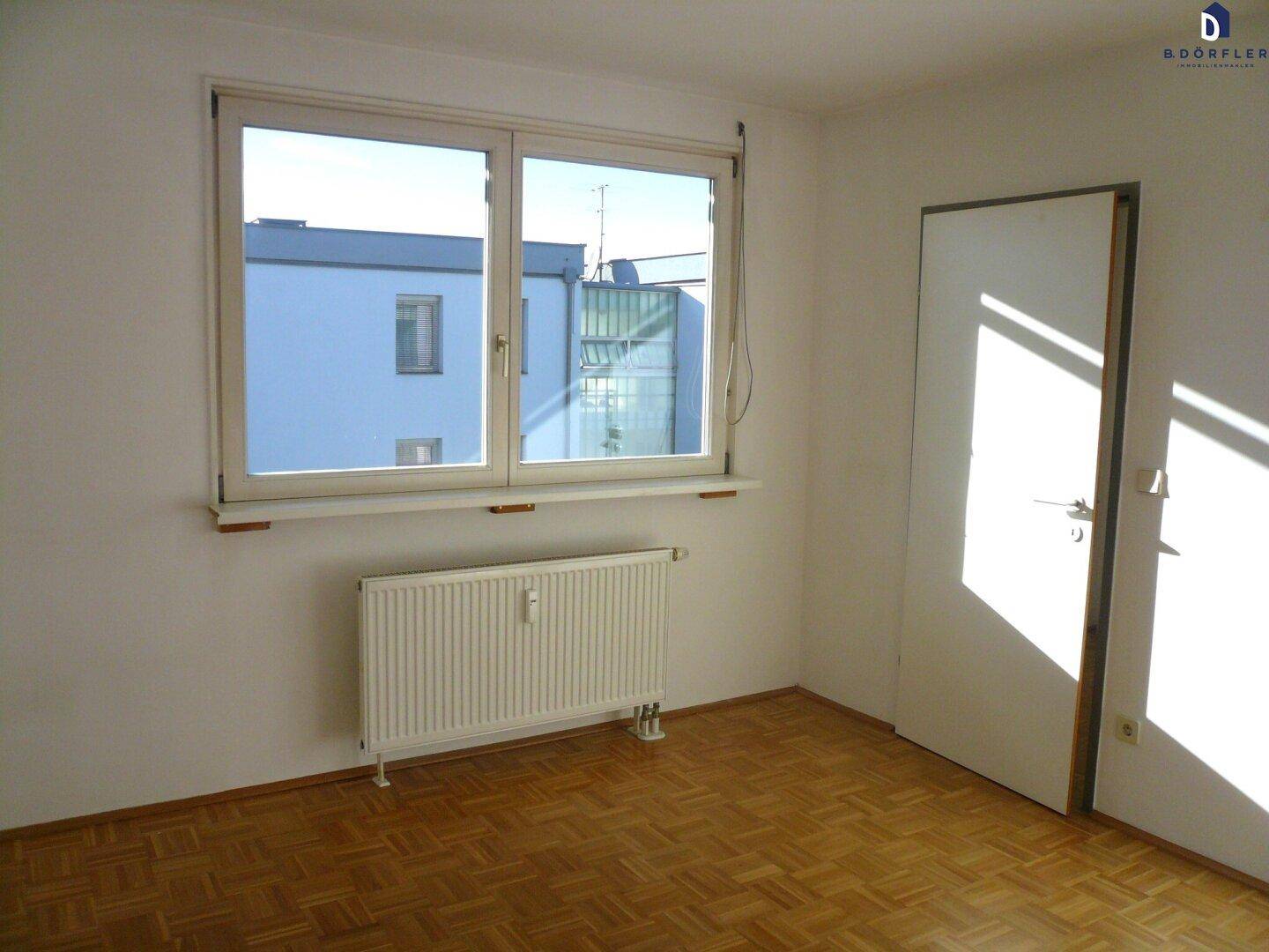 Heller Raum mit Parkettboden, Fenster und Heizkörper.