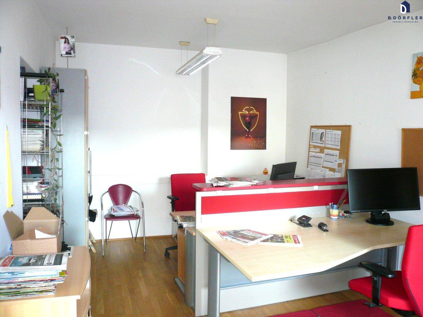 Moderner Bürobereich mit roten Akzenten, mehreren Arbeitsplätzen und Regalen für Akten und Büromaterial.