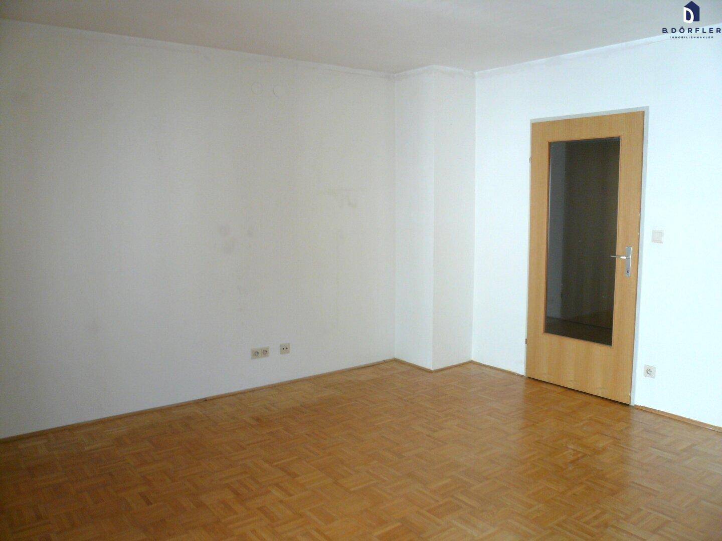 Leeres Zimmer mit Parkettboden und einer Holztür mit Glaseinsatz, bereit zur individuellen Gestaltung.