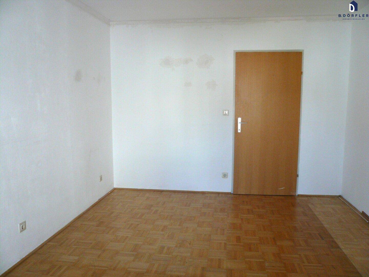 Heller Raum mit Parkettboden und einer einfachen Holztür, ideal für verschiedene Wohnzwecke.