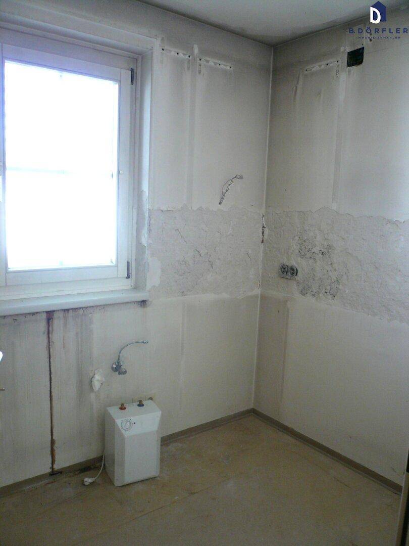 Unfertige Küche mit Fenster und vorbereiteten Anschlüssen, bereit für den Einbau einer neuen Küchenzeile.