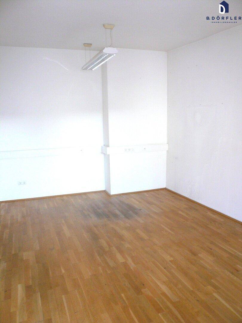 Leerer Büroraum mit Parkettboden und weißen Wänden, bereit zur Einrichtung.