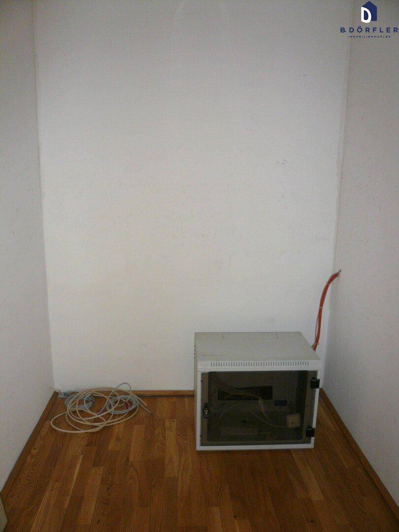 Kleiner Abstellraum mit Parkettboden und einem Netzwerkschrank in der Ecke.