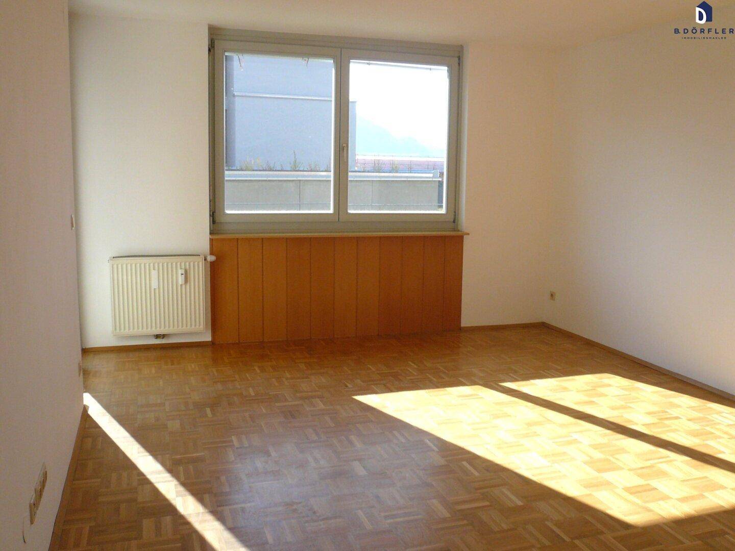 Heller Wohnraum mit Parkettboden, Holzvertäfelung und großem Fenster, durchflutet von Sonnenlicht.