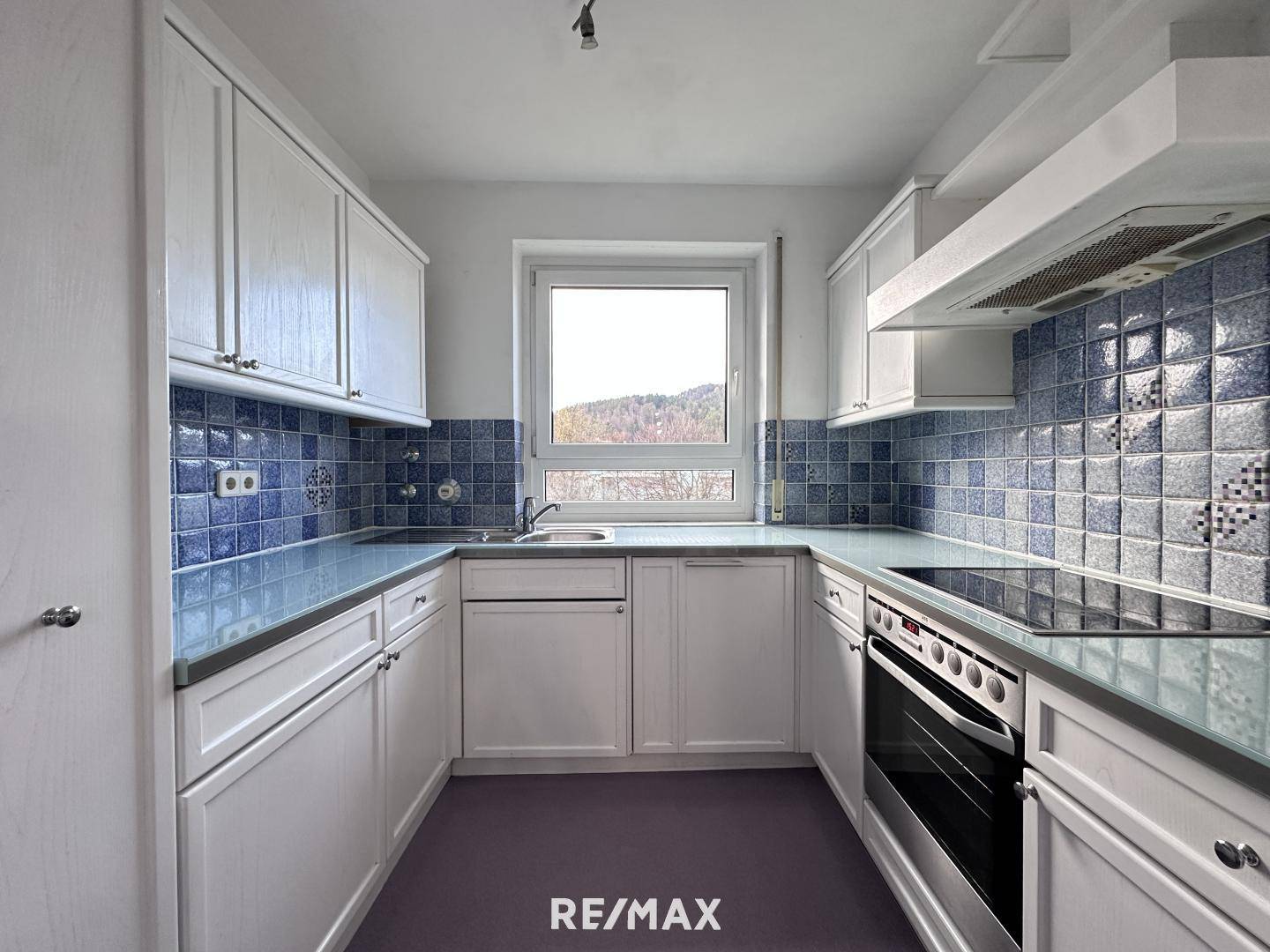 Funktionale Küche mit weißen Schränken, blauen Fliesen und Blick ins Grüne.