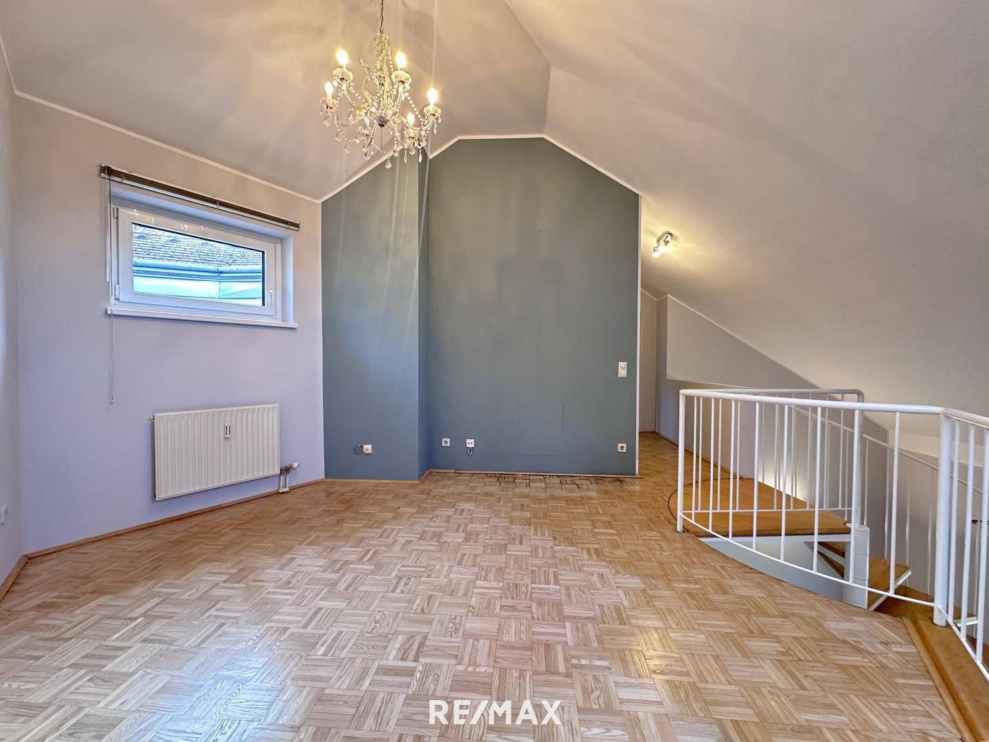 Gemütlicher Raum im Dachgeschoss mit schrägen Decken, Parkettboden und einem Fenster.