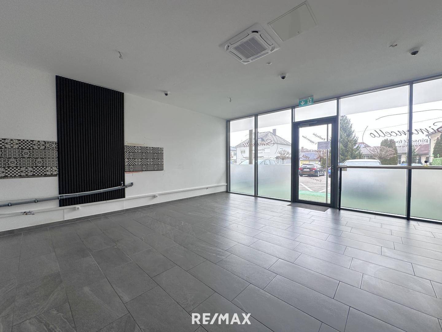 Heller Gewerberaum mit großen Fenstern, modernen Fliesen und einer dekorativen schwarzen Wandverkleidung.