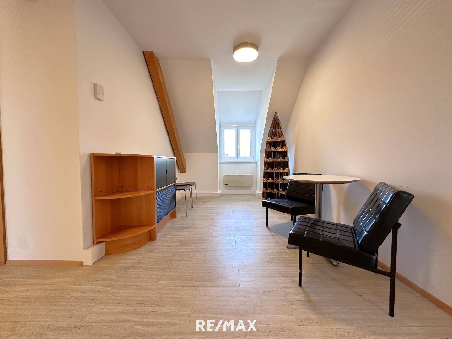 Gemütlicher Raum im Dachgeschoss mit schrägen Wänden, einem Fenster und einer kleinen Sitzecke, ideal für Pausen oder Empfang.