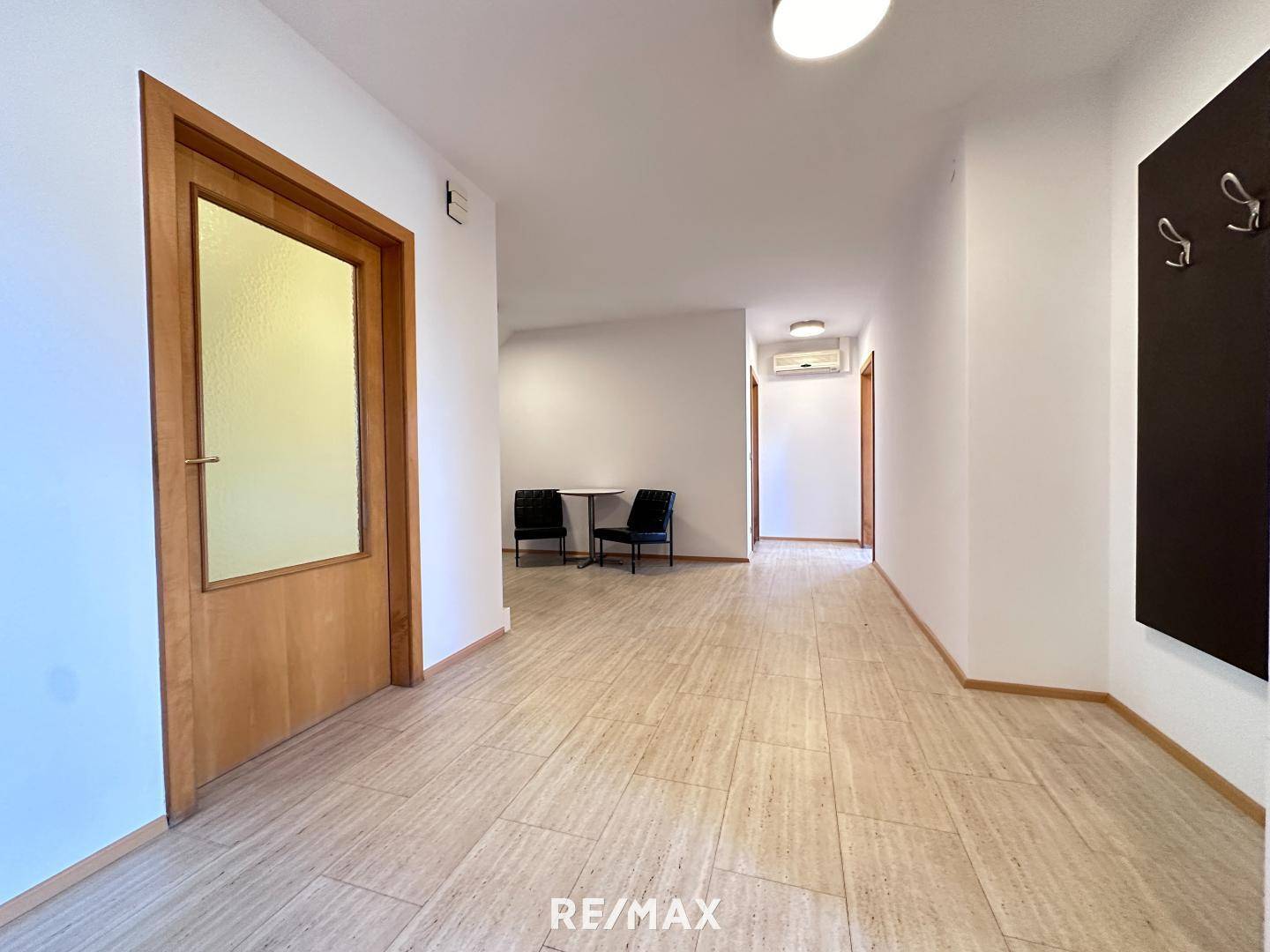 Geräumiger Flur mit hellen Fliesen, Holztüren und einem kleinen Sitzbereich, der zu weiteren Räumen führt.