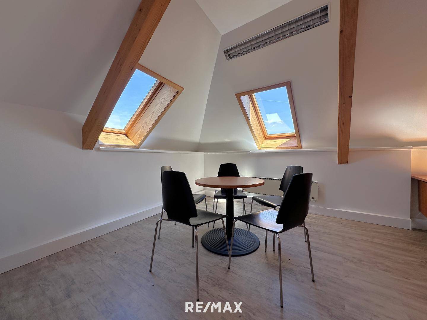 Heller Aufenthaltsraum im Dachgeschoss mit schrägen Wänden, Dachfenstern und einem kleinen Tisch mit Stühlen.
