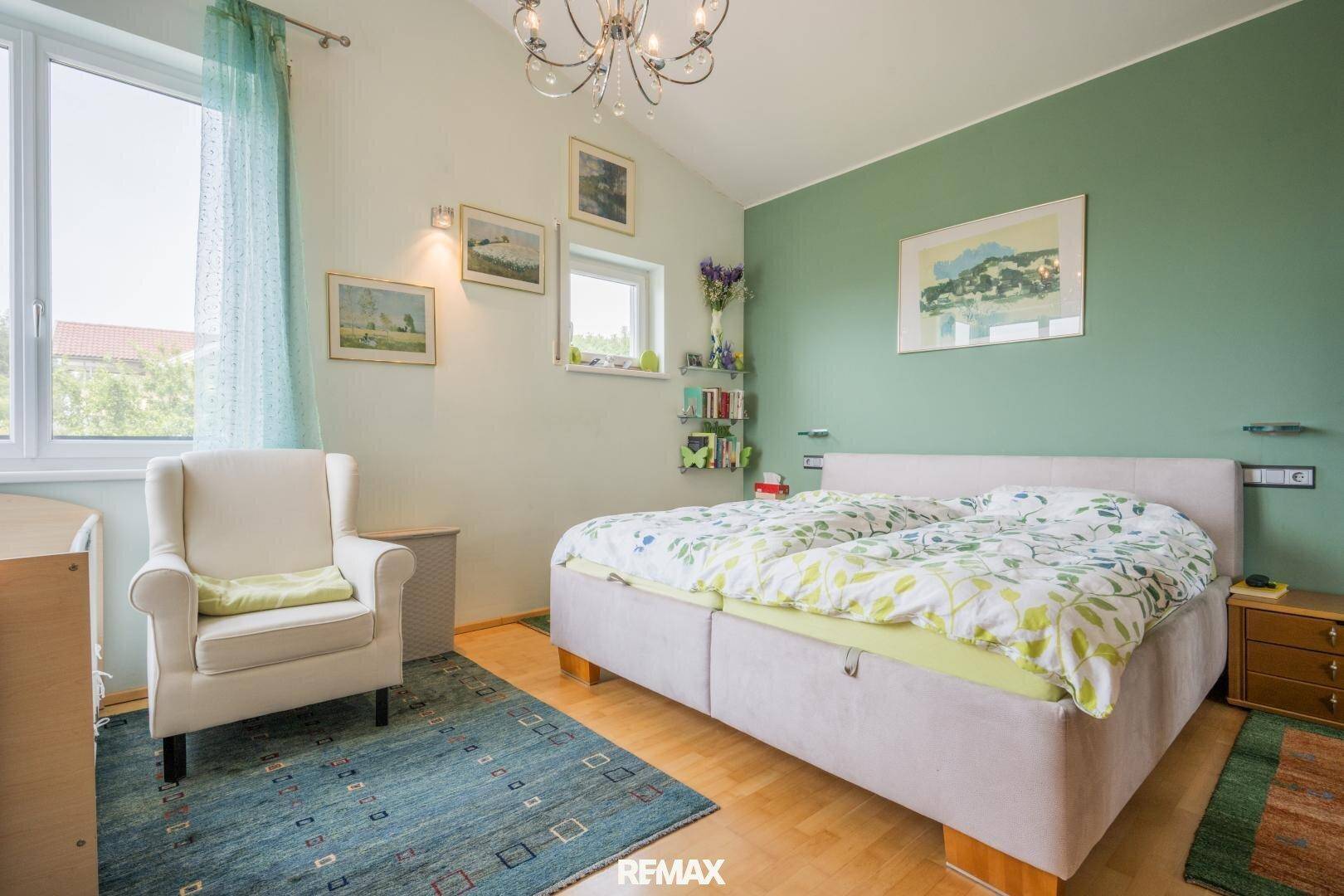 Gemütliches Schlafzimmer mit grüner Akzentwand, Doppelbett und hellem Holzfußboden.