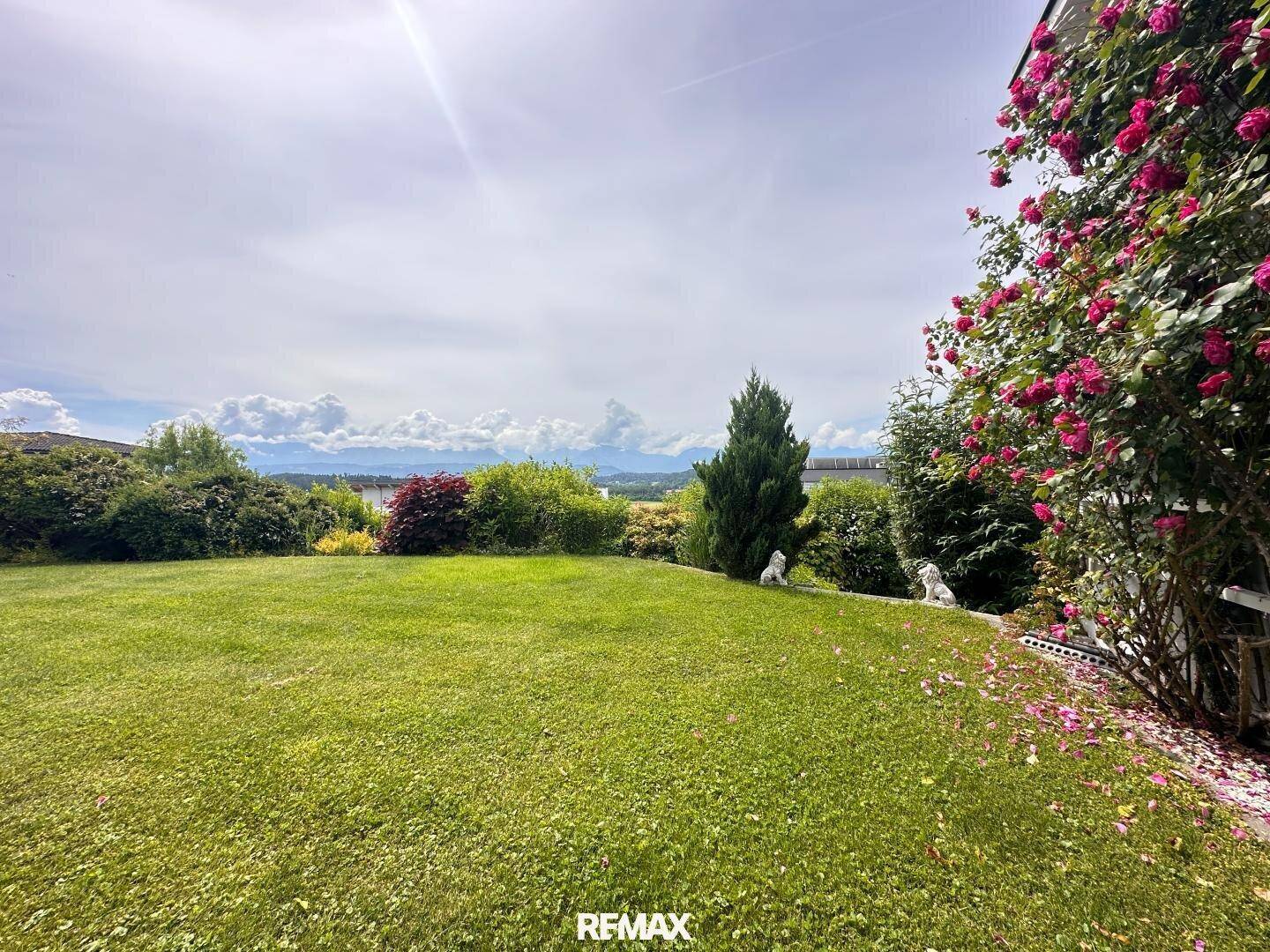 Grüner Garten mit Rasenfläche, blühenden Rosensträuchern und einem weiten Blick in die Landschaft.