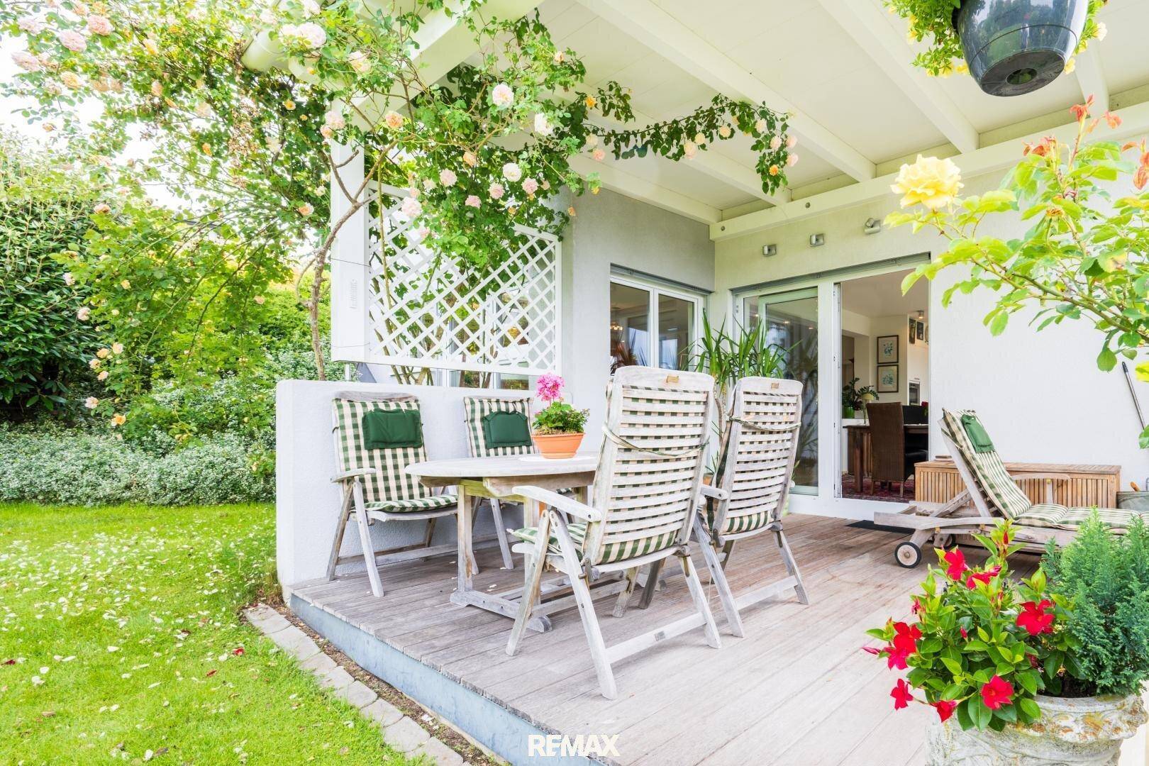 Holzterrasse mit Gartenmöbeln und direktem Zugang zum blühenden Garten mit Rosensträuchern.