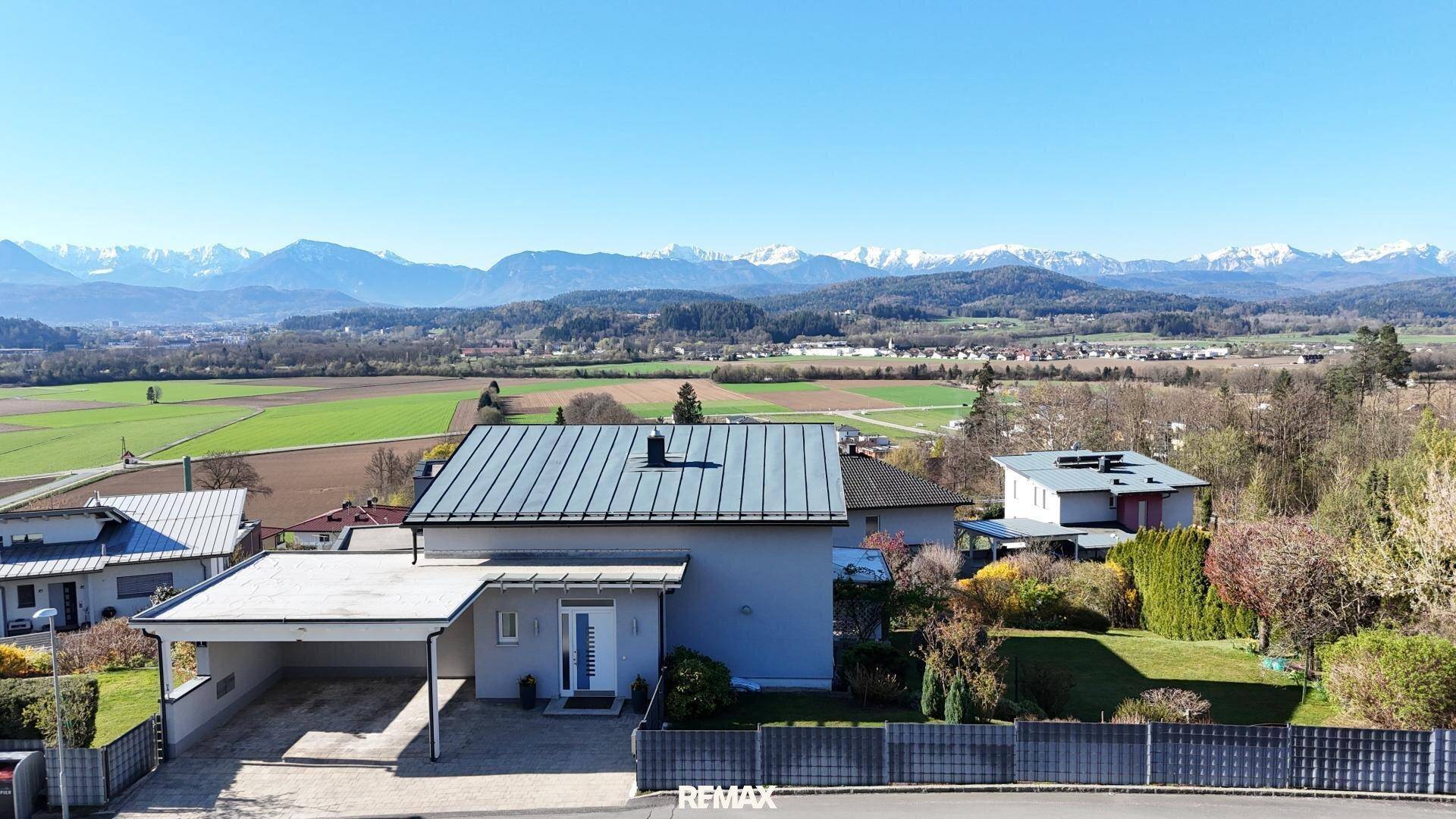 Modernes Einfamilienhaus mit Carport, gepflegtem Rasen und beeindruckendem Bergblick in der Ferne.