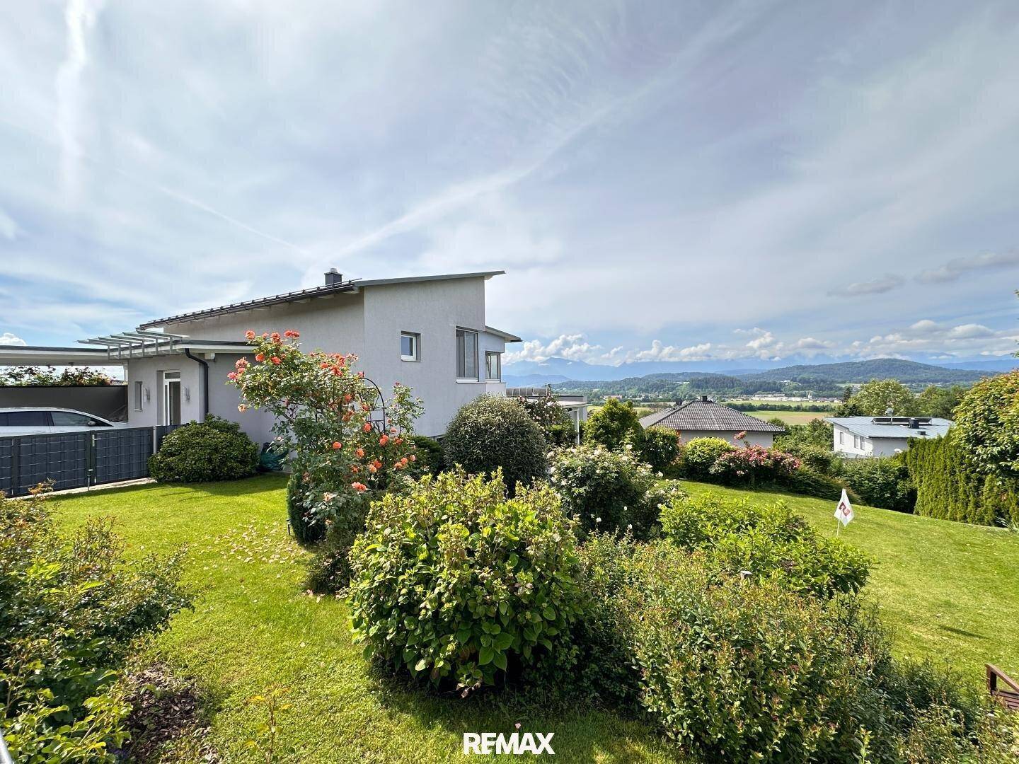 Gepflegter Garten mit Rasenfläche und Sträuchern, im Hintergrund ein Haus und Bergblick.