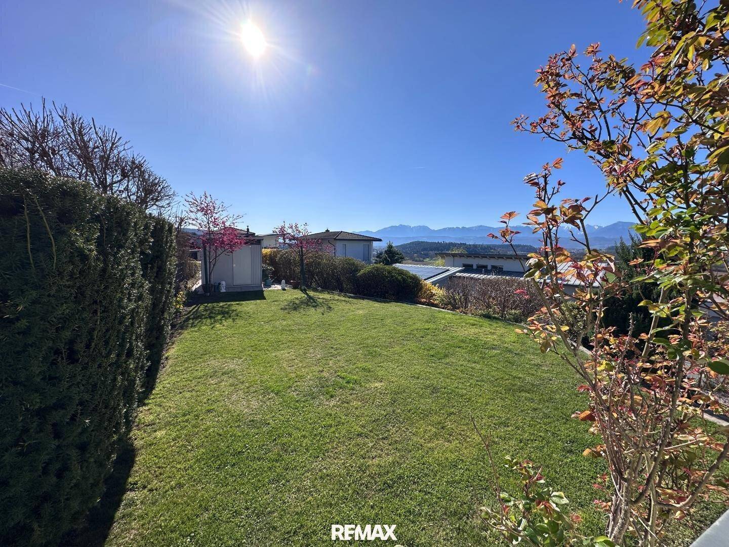 Sonniger Garten mit Rasenfläche, kleinem Geräteschuppen und weitem Blick auf die Berge.