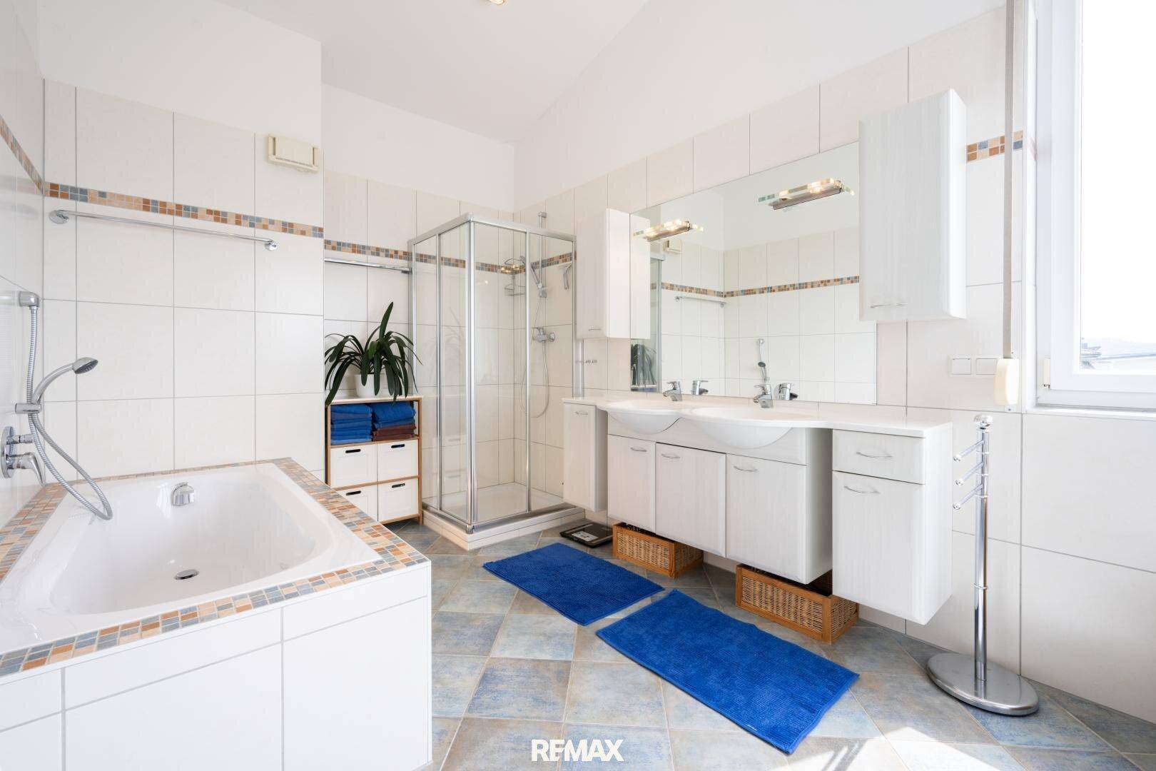 Helles Badezimmer mit Badewanne, Duschkabine, Doppelwaschbecken und weißen Fliesen.
