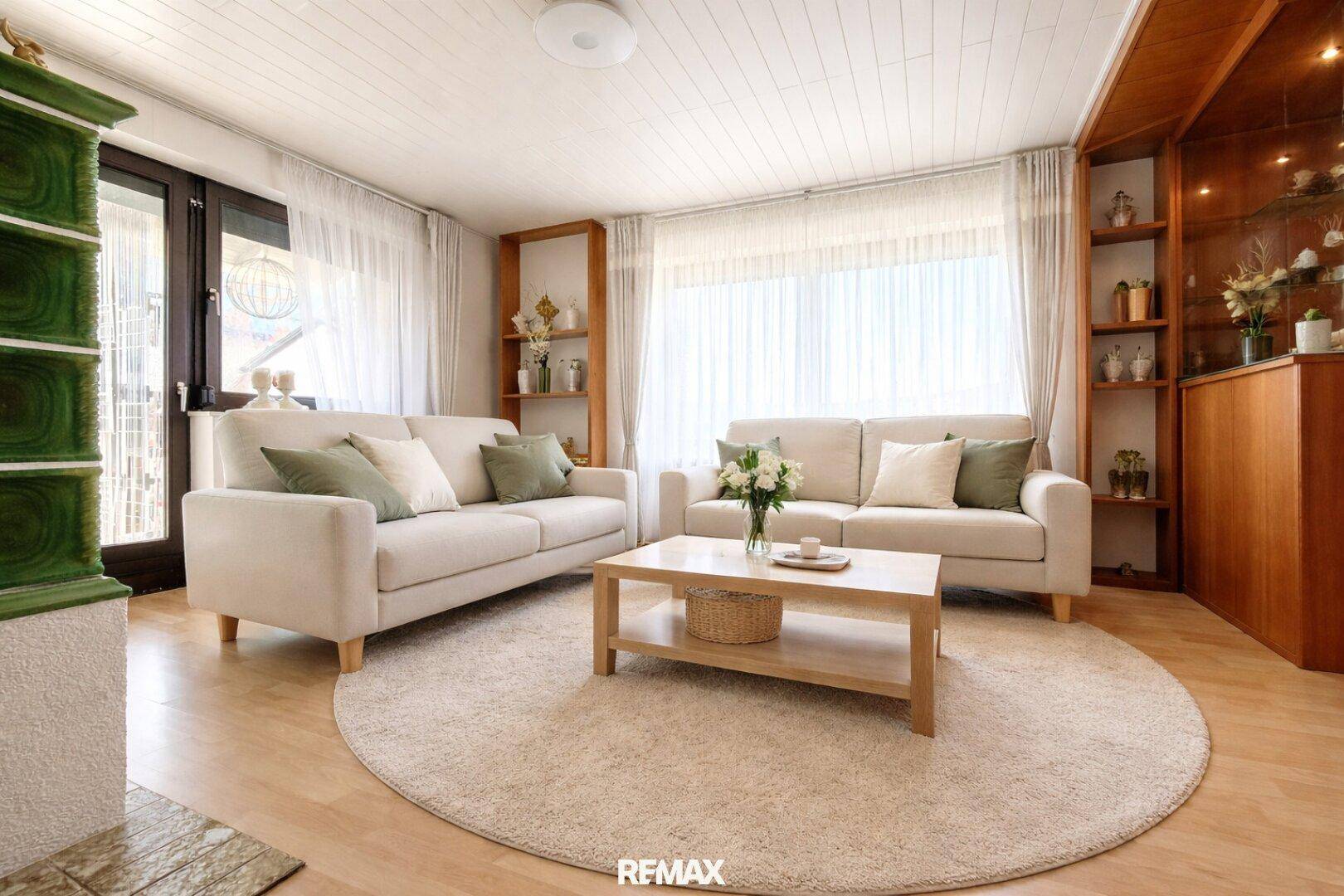 Gemütliches Wohnzimmer mit beigen Sofas, Laminatboden und einem traditionellen Kachelofen.