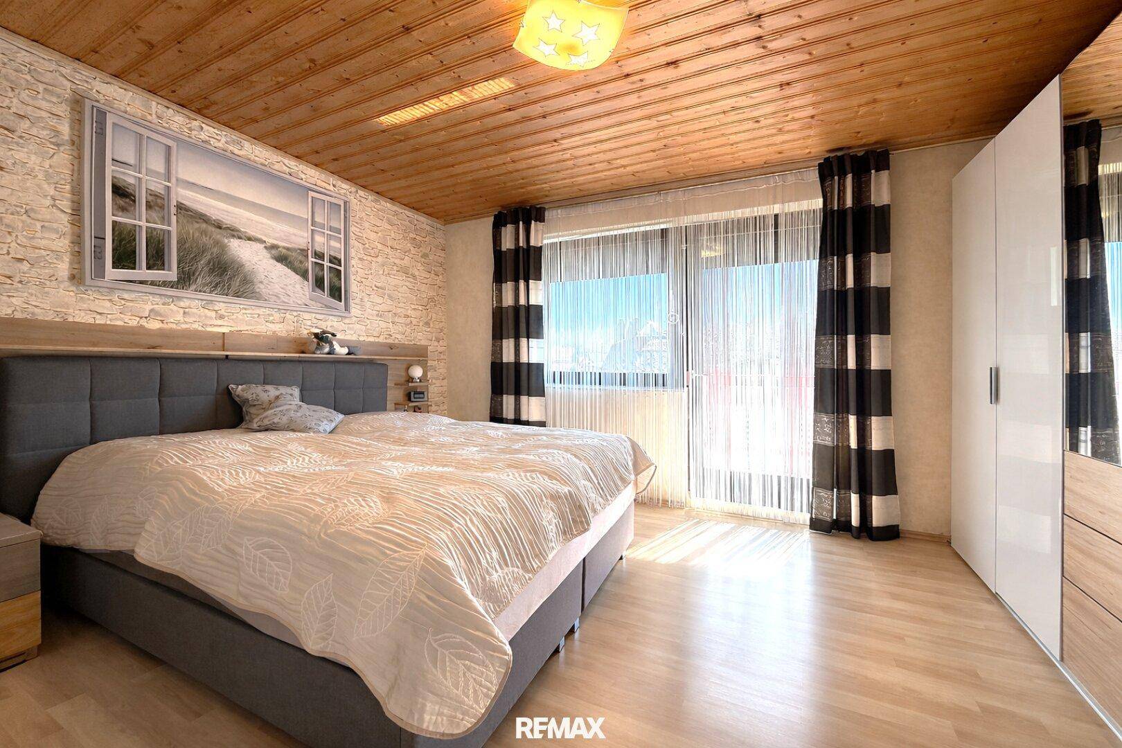 Helles Schlafzimmer mit Doppelbett, Holzdecke und Zugang zum Balkon.