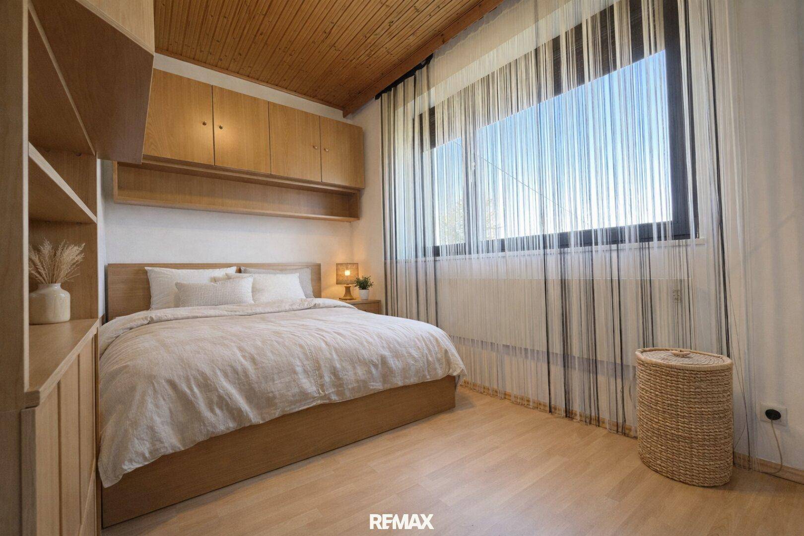 Schlafzimmer mit Doppelbett, Holzdecke, Laminatboden und großem Fenster.