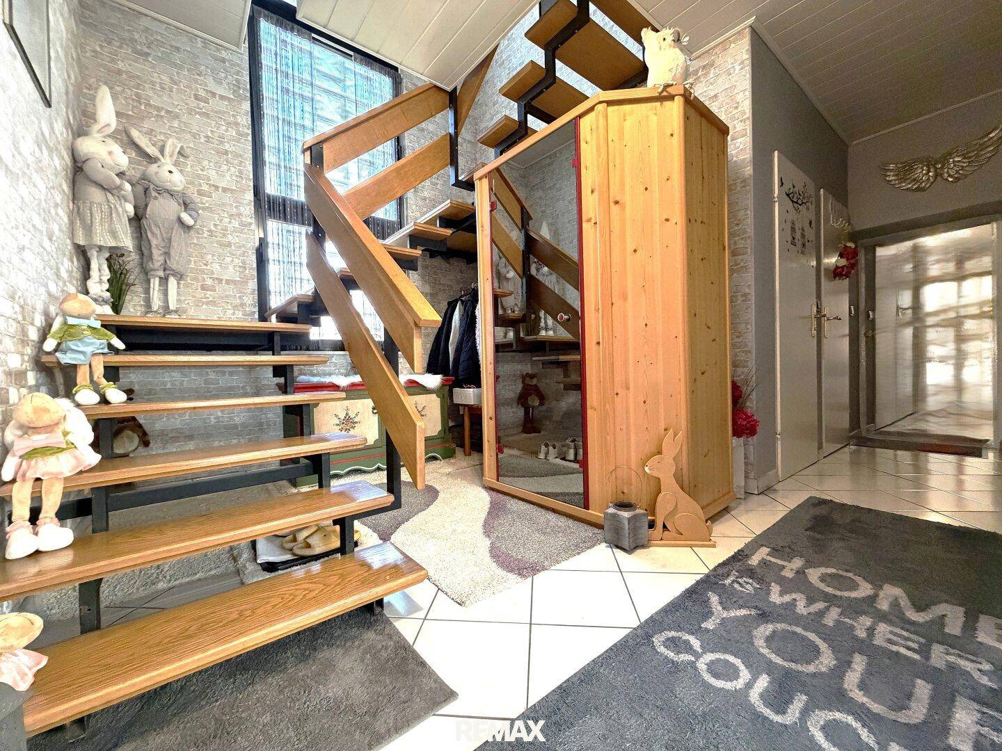 Geräumiger Flur mit offener Holztreppe, Fliesenboden und dekorativen Elementen.