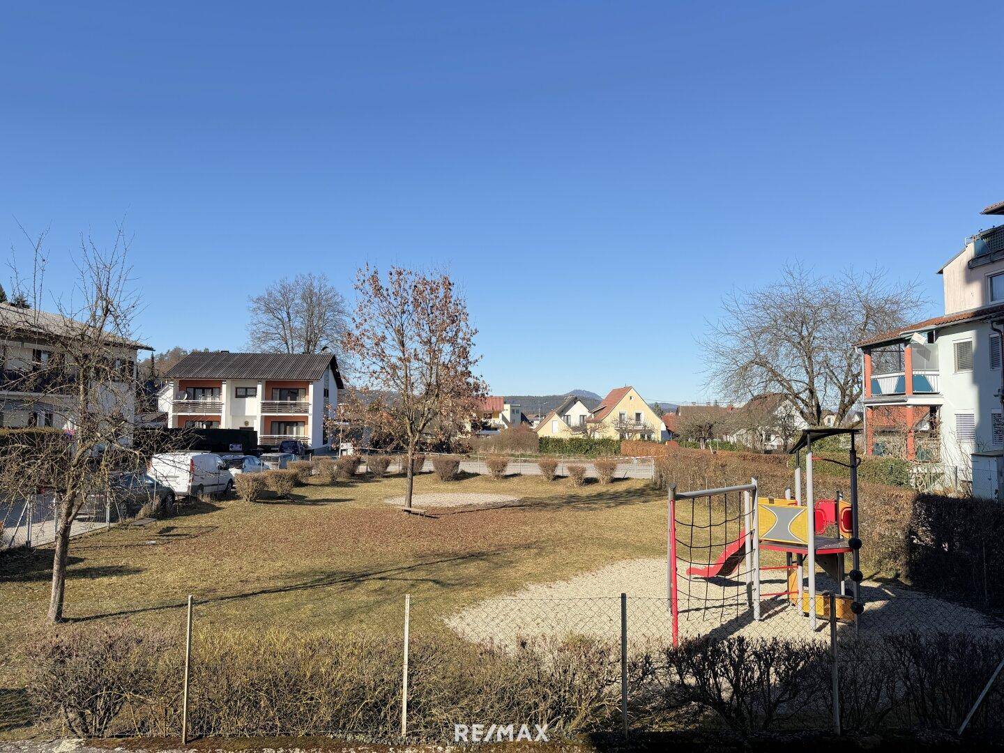 Blick auf einen sonnigen Spielplatz und die umliegende Wohnbebauung in ruhiger Lage.
