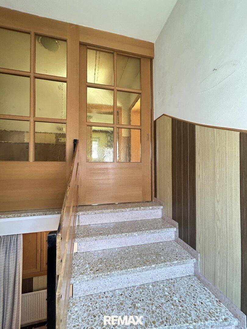 Treppenhaus mit Terrazzostufen und Holzvertäfelung, das zu den oberen Etagen führt.
