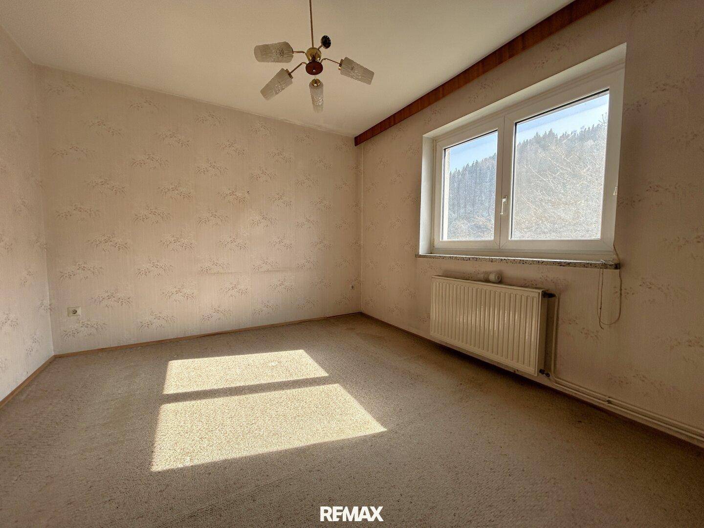 Geräumiges Schlafzimmer mit Teppichboden, Tapeten und einem großen Fenster.