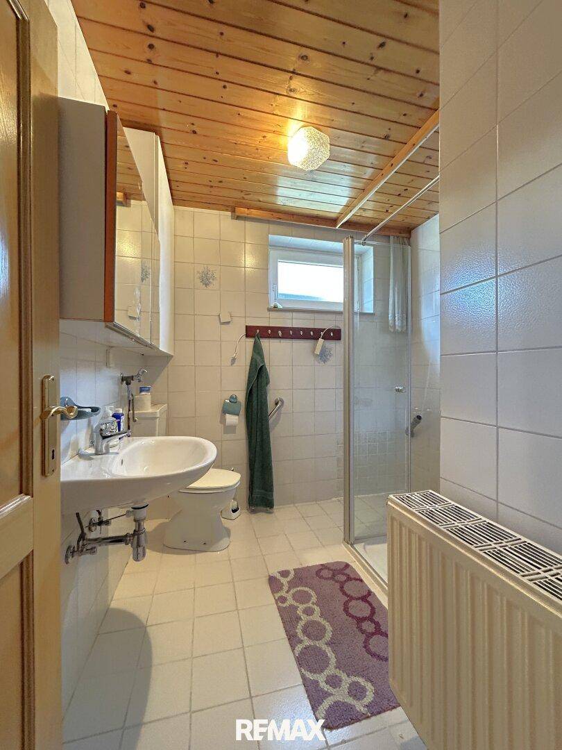Badezimmer mit weißen Fliesen, Holzdecke, Dusche und Fenster für Tageslicht.