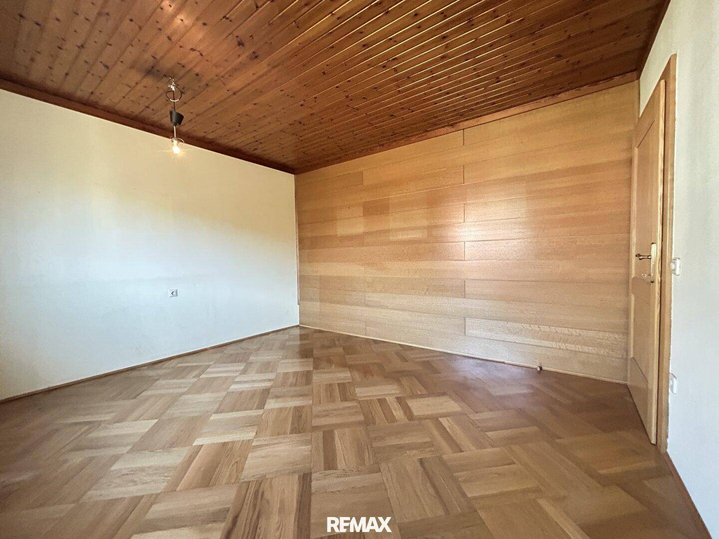 Helles Wohnzimmer mit Parkettboden, Holzdecke und einer Holzwand.