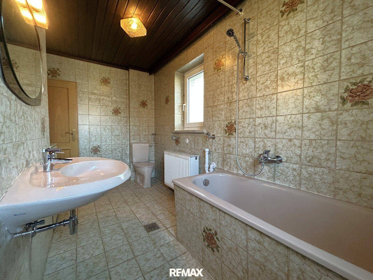 Badezimmer mit gemusterten Fliesen, Badewanne und Fenster für natürliche Belüftung.