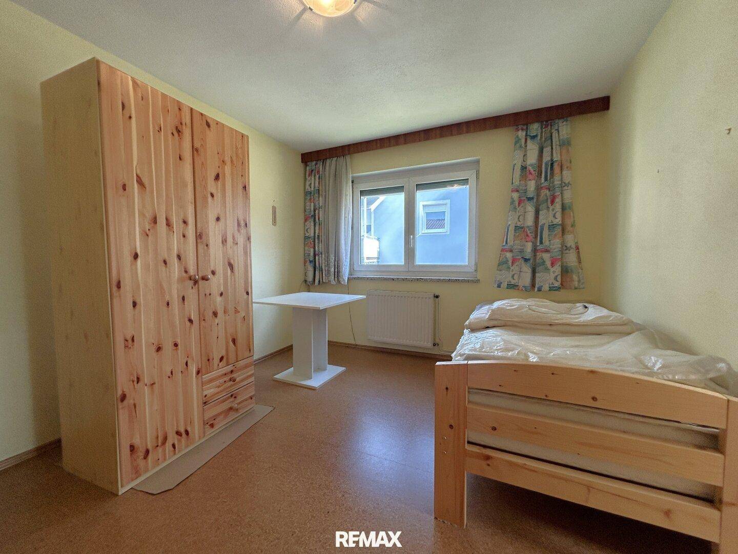 Schlafzimmer mit Korkboden, Holzschrank und Fenster mit Blick ins Grüne.