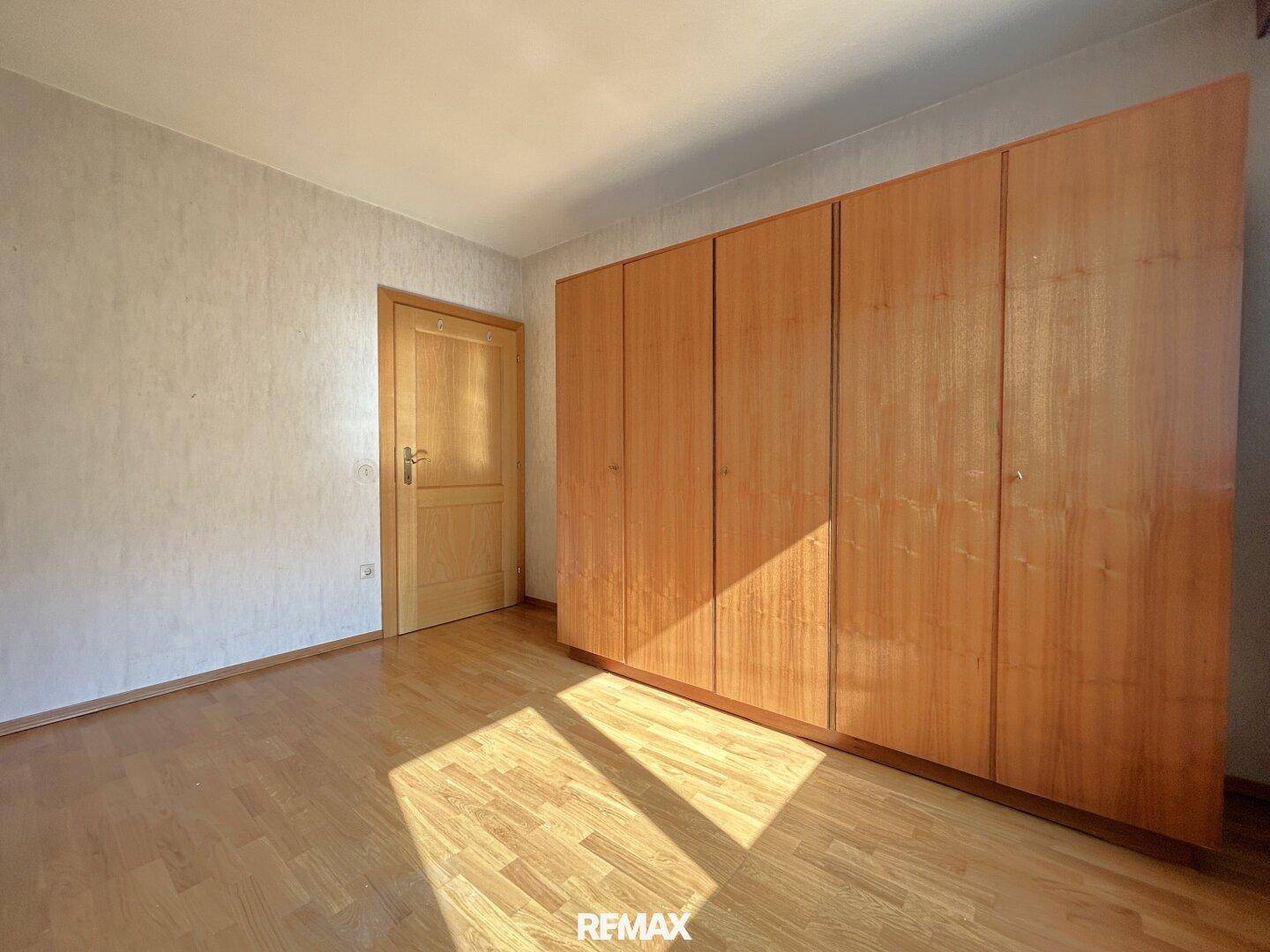 Schlafzimmer mit Holzboden, Tapeten und einem großen Einbauschrank aus Holz.