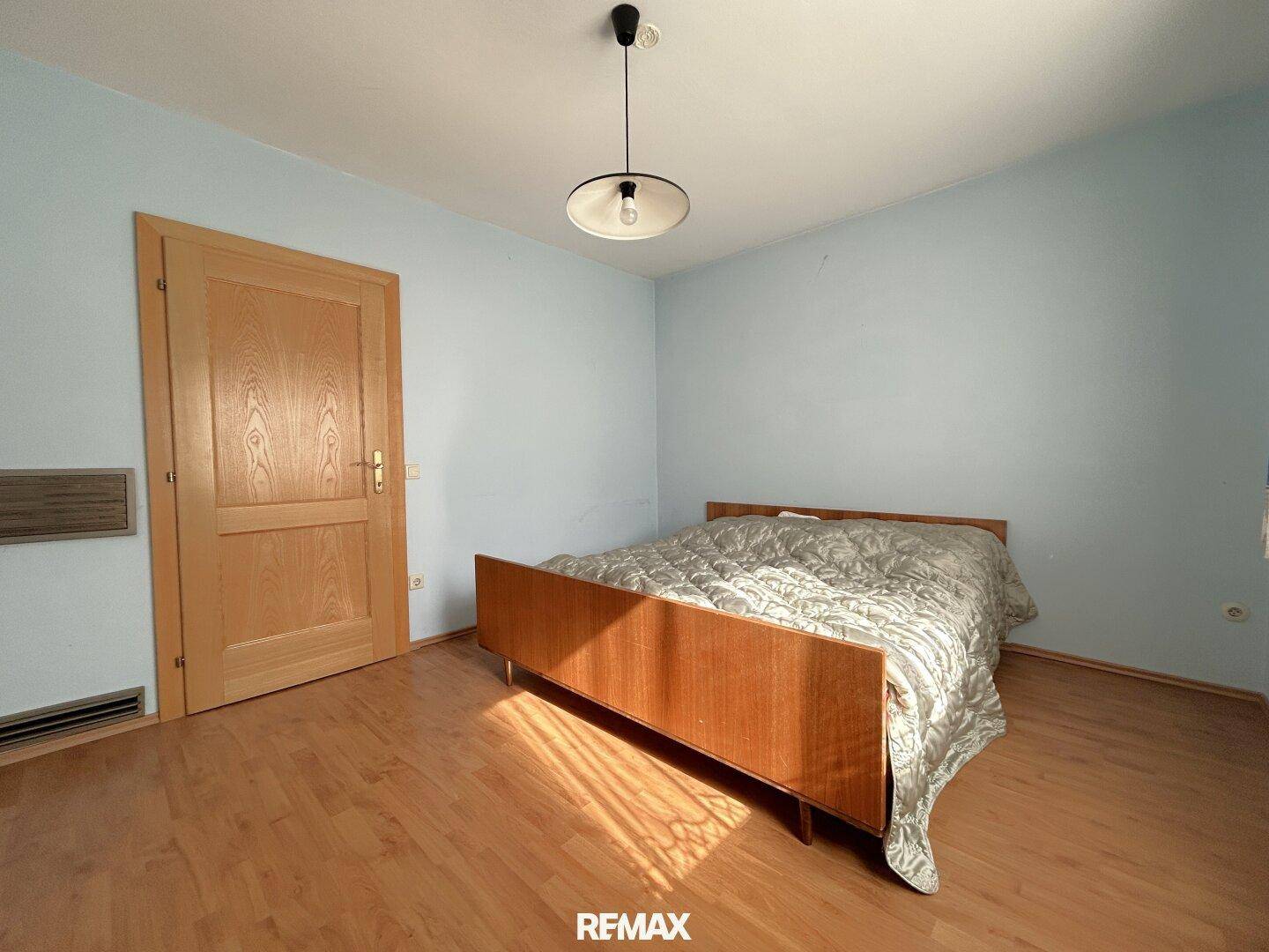 Schlafzimmer mit Holzboden, hellblauen Wänden und einem einfachen Bettgestell.