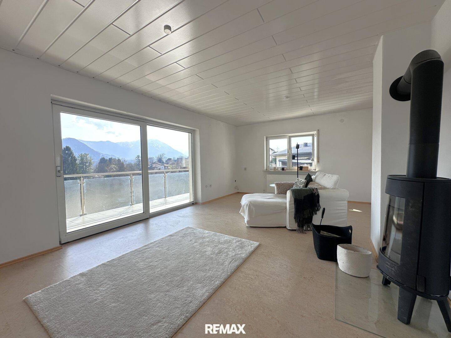 Helles Wohnzimmer mit Kaminofen, Zugang zum Balkon und Bergblick durch große Schiebetüren.