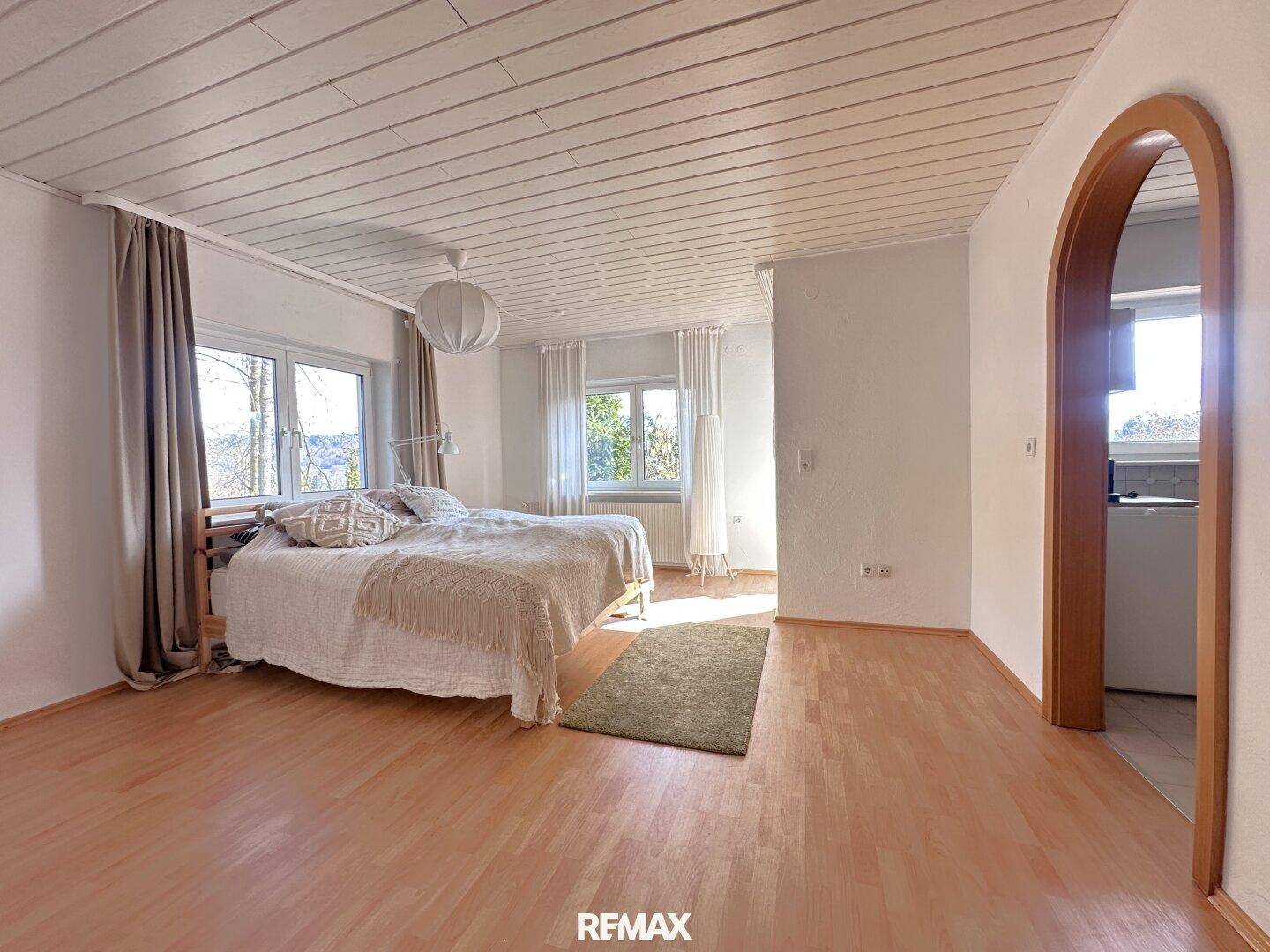 Gemütliches Schlafzimmer mit Doppelbett, Holzbalkendecke und viel Tageslicht durch mehrere Fenster.