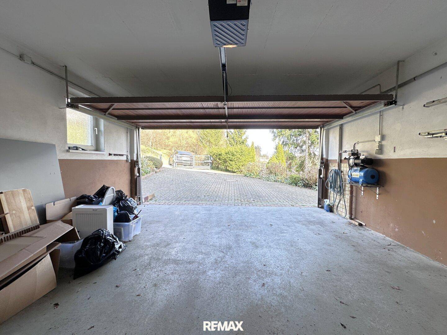 Geräumige Garage mit Betonboden und Blick auf die gepflasterte Auffahrt und die grüne Umgebung.