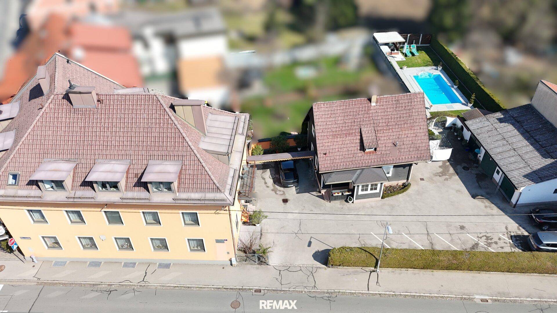 Luftaufnahme eines Gebäudekomplexes mit Parkplätzen und einem Schwimmbad im hinteren Bereich.