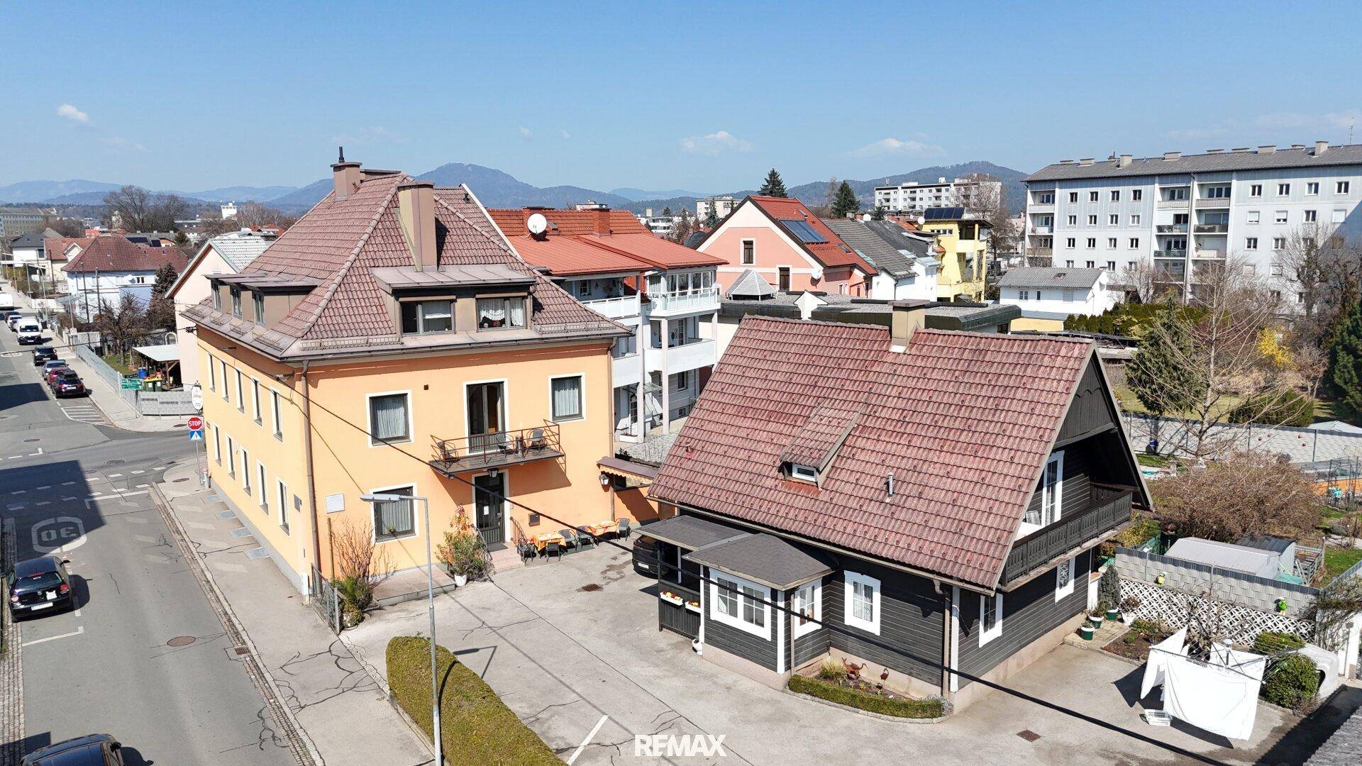 Luftaufnahme von zwei Gebäuden mit einem Parkplatz und Bergen im Hintergrund unter blauem Himmel.