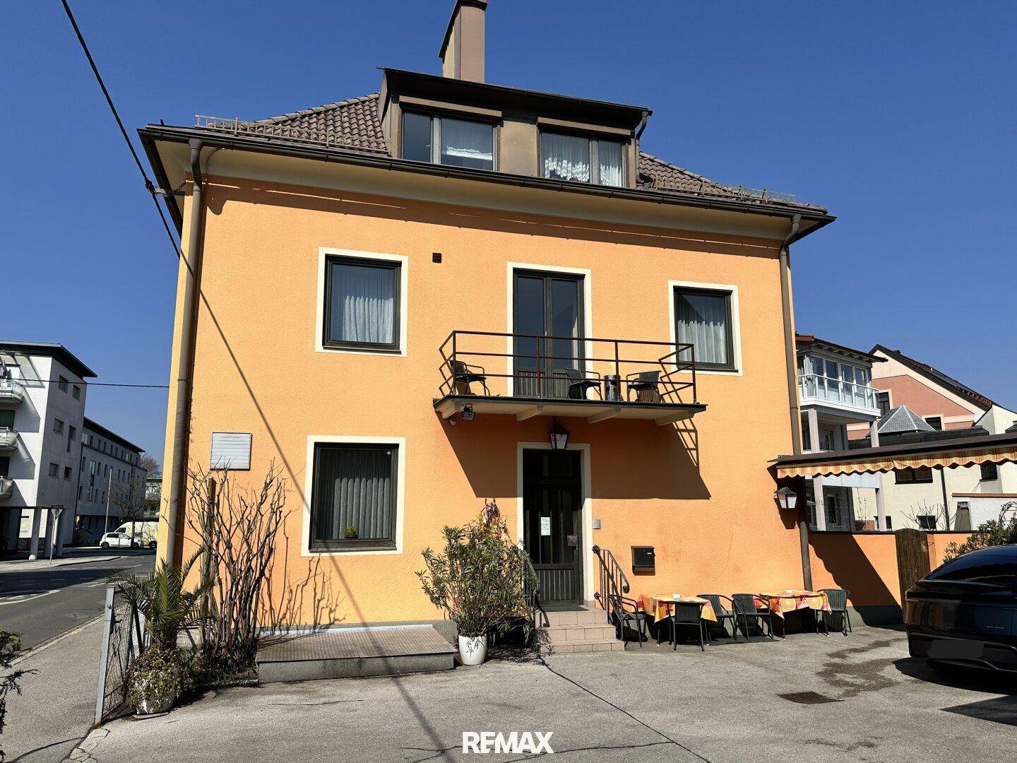 Vorderansicht eines orangefarbenen Gebäudes mit Balkon, Fenstern und einem Eingangsbereich.