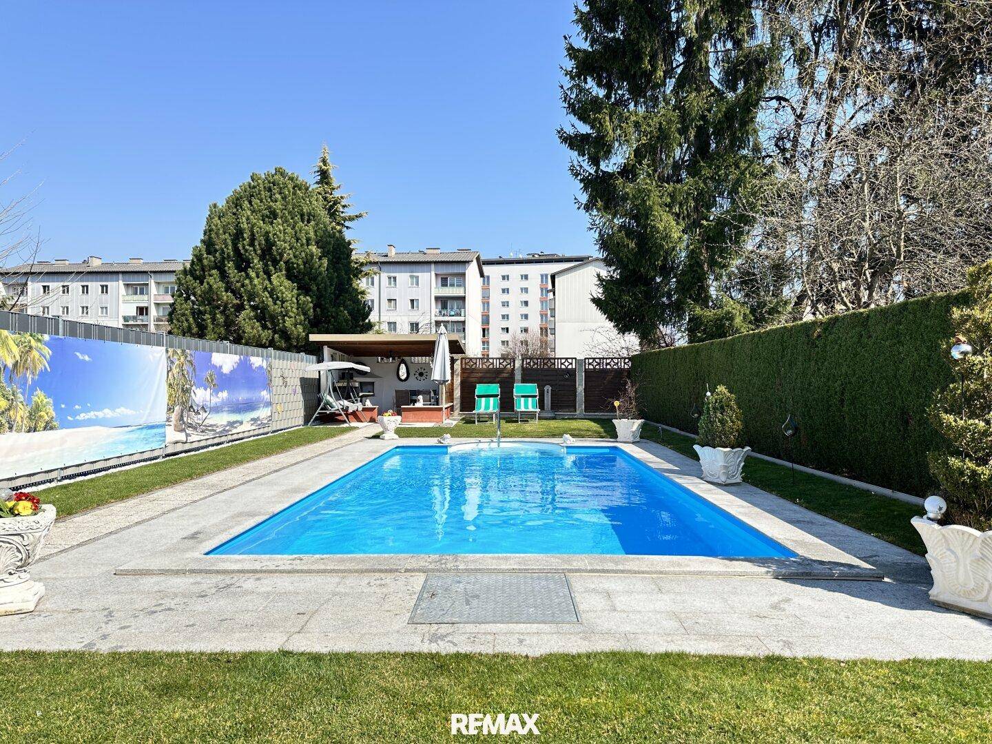 Großer, rechteckiger Pool in einem gepflegten Gartenbereich mit Rasen und hohen Hecken.