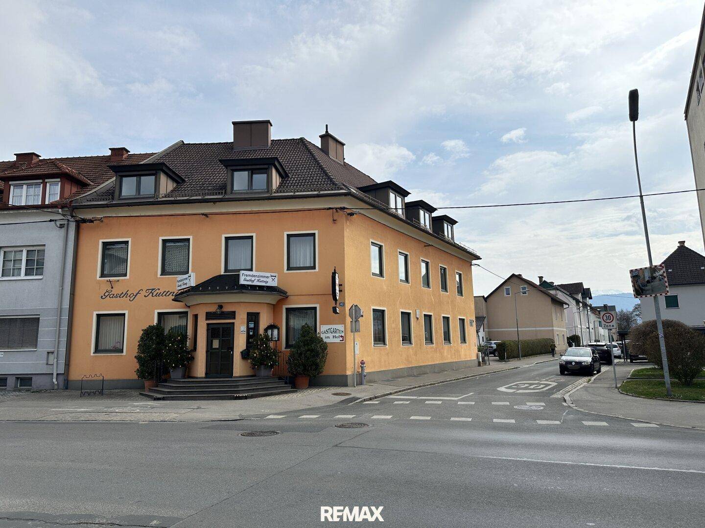 Straßenansicht eines orangefarbenen Gebäudes mit mehreren Fenstern und einem Eingangsbereich an einer Kreuzung.