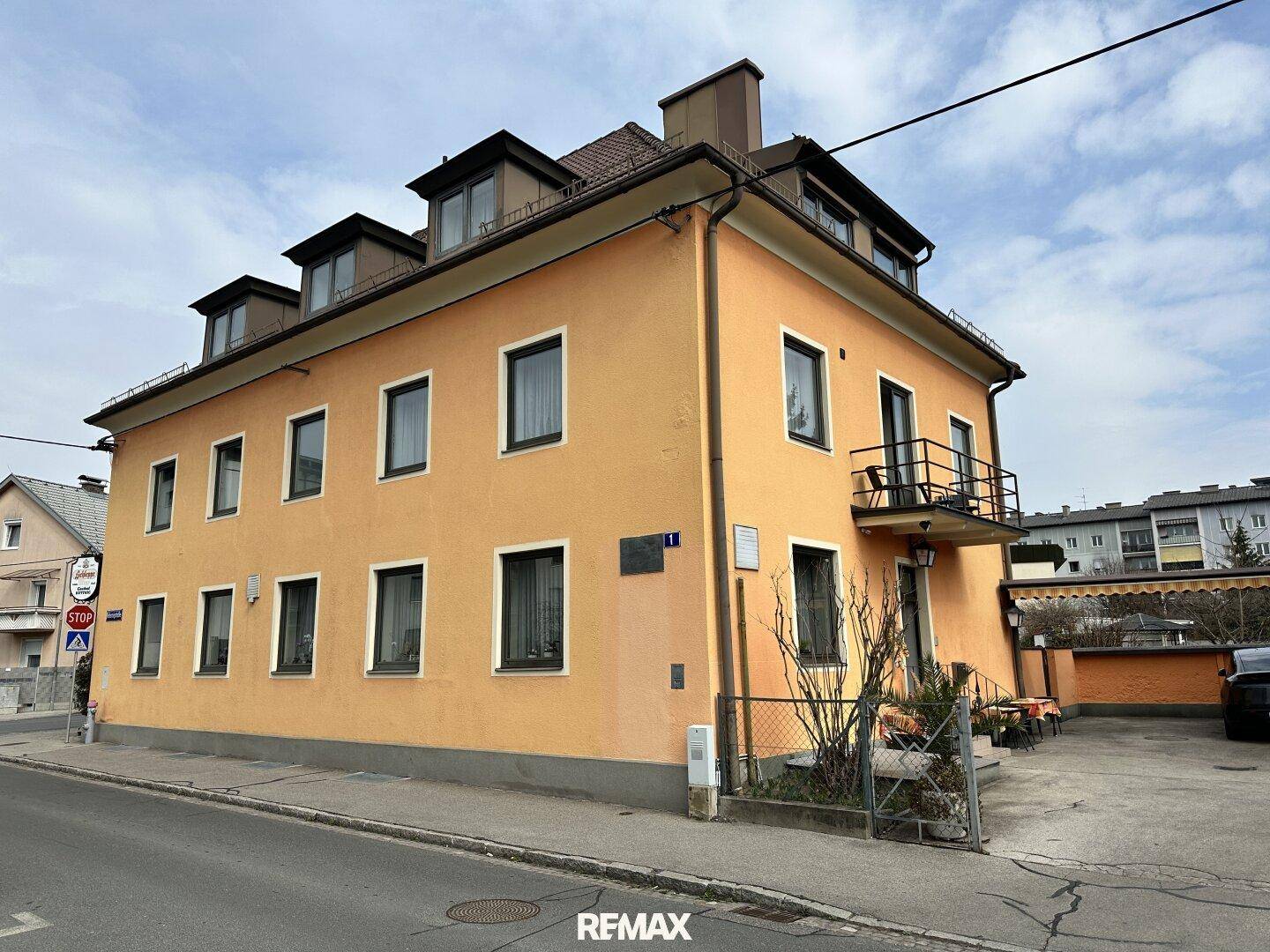 Seitenansicht eines orangefarbenen Gebäudes mit Fenstern, einem kleinen Balkon und einem Zaun.