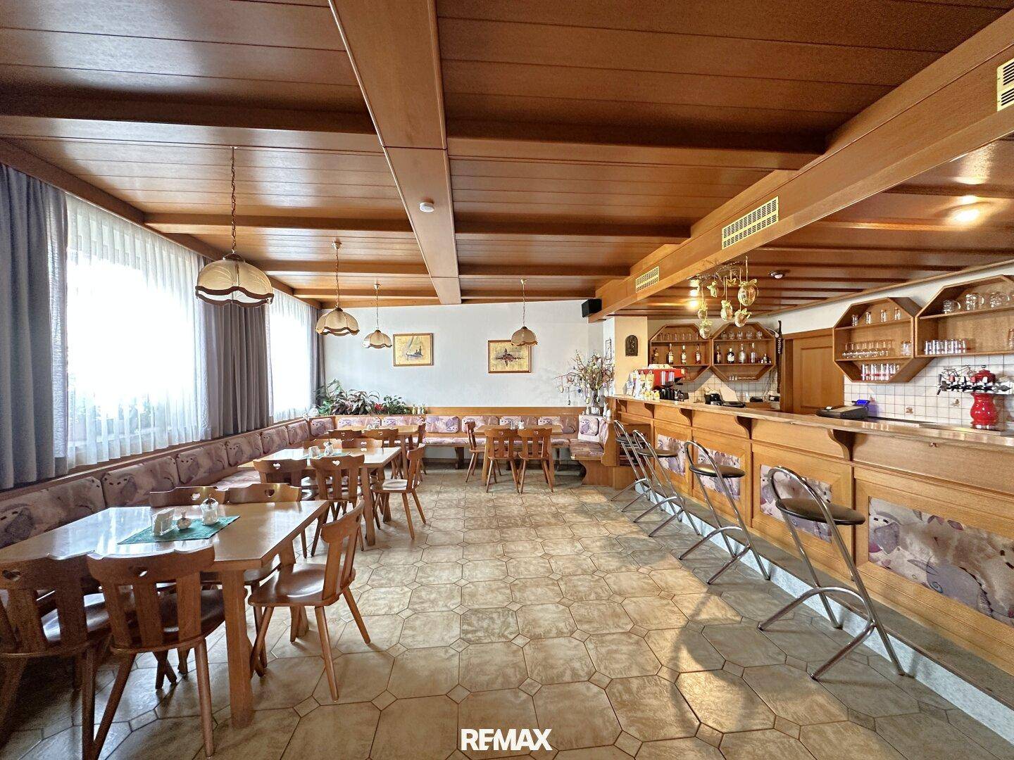 Traditioneller Gastraum mit Holzbalkendecke, Tischen, Bänken und einer Bar im Hintergrund.
