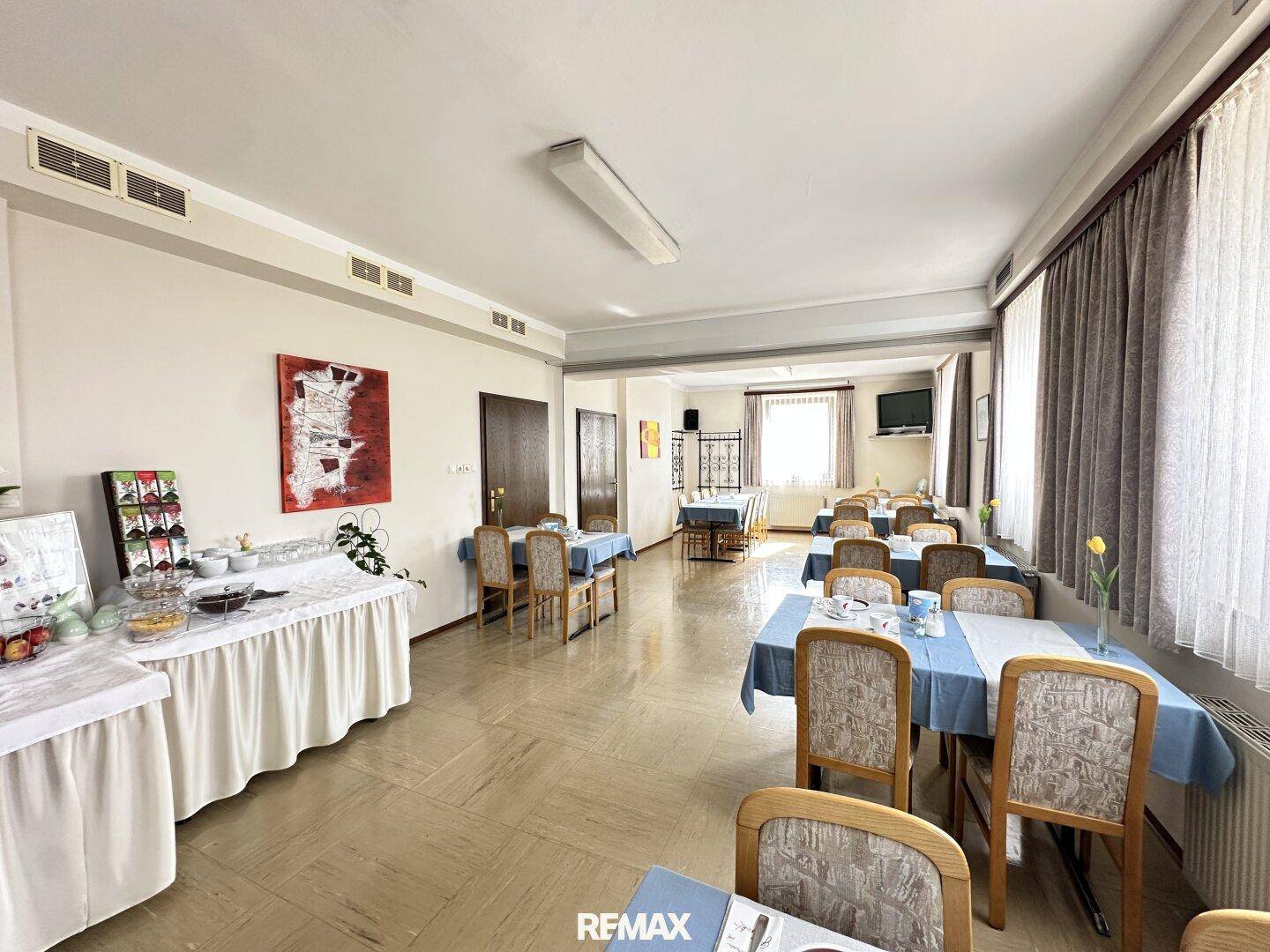 Heller Frühstücksraum mit mehreren Tischen, Stühlen und einem Buffetbereich.