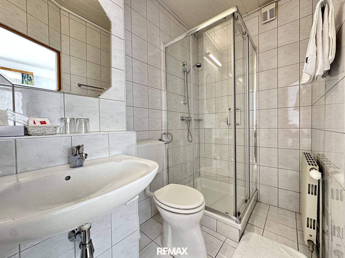 Gefliestes Badezimmer mit Duschkabine, WC und Waschbecken in hellem Design.