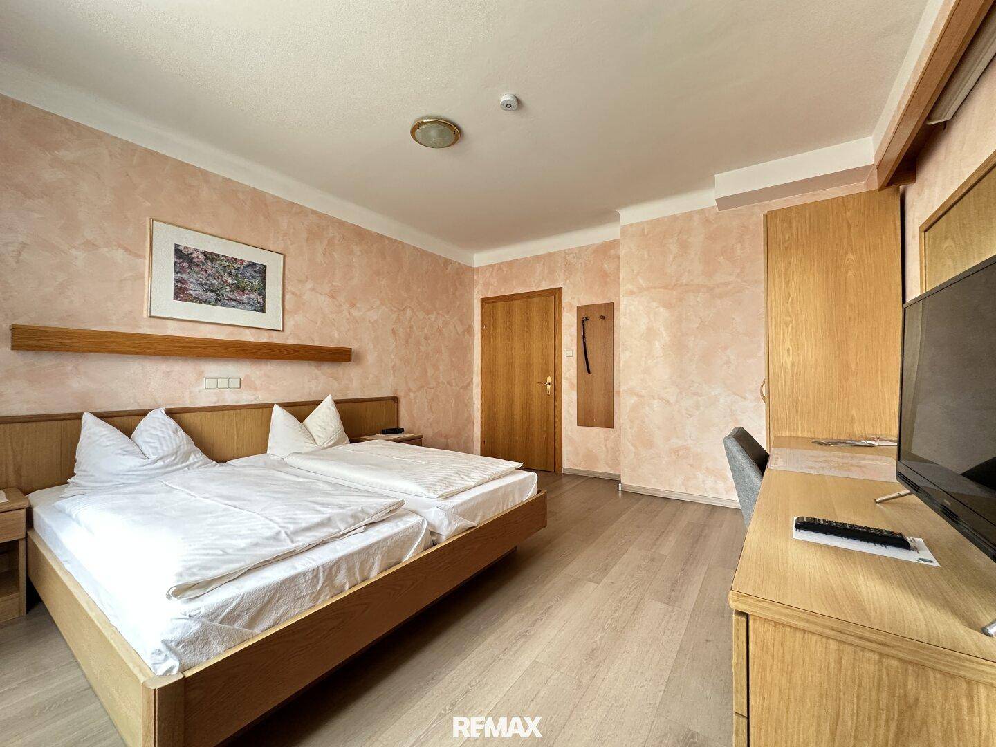 Komfortables Schlafzimmer mit Doppelbett, Holzmöbeln und Laminatboden in warmen Farbtönen.