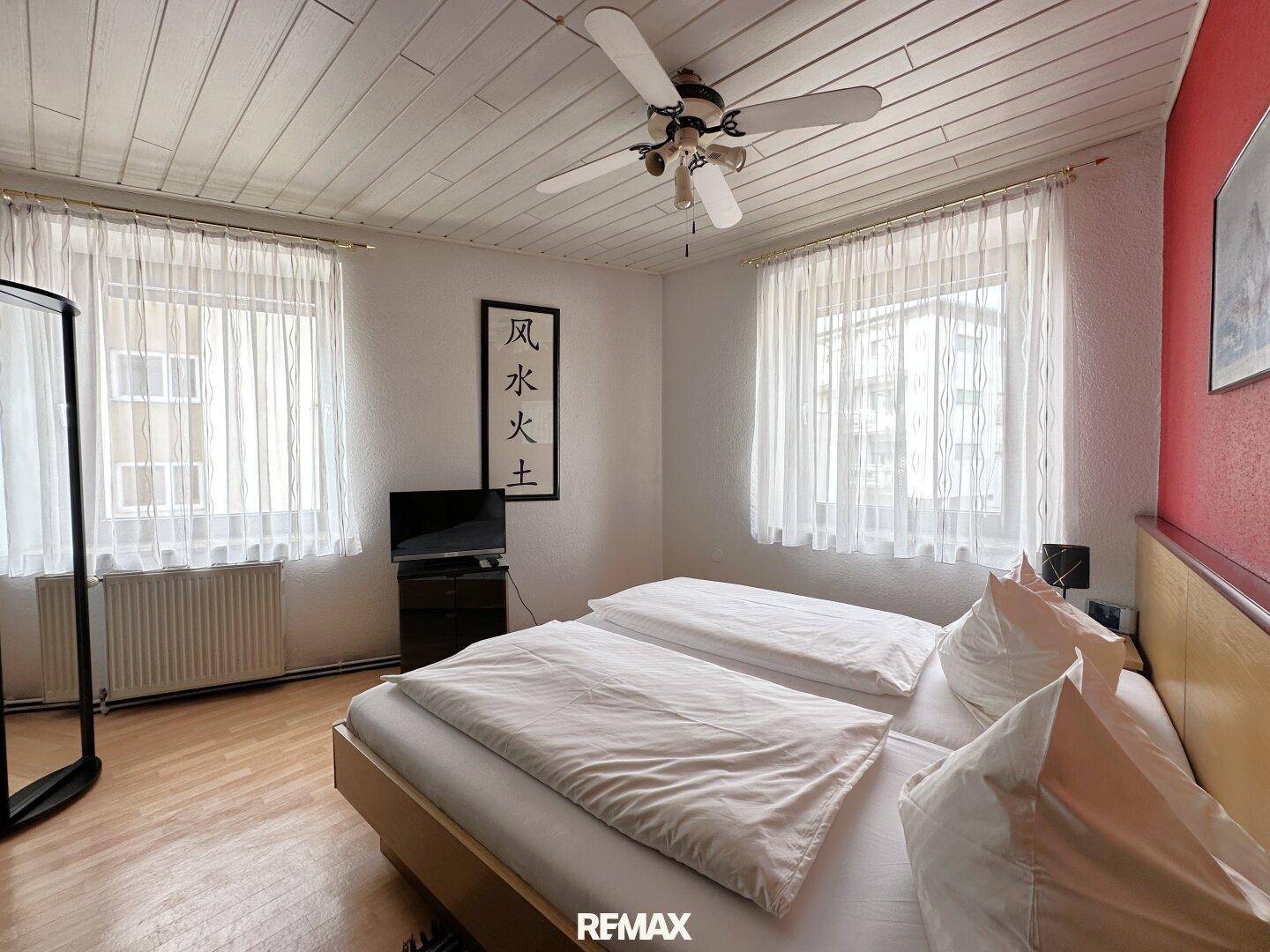 Schlafzimmer mit Doppelbett, Deckenventilator, Holzdecke und Laminatboden.